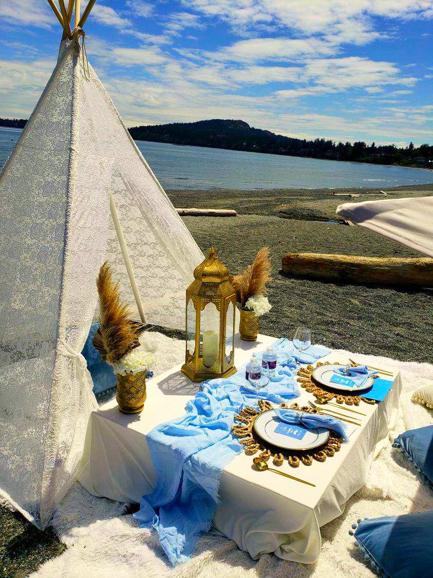 Lace teepee beach picnic with dusty-blue linen and hills across the water
