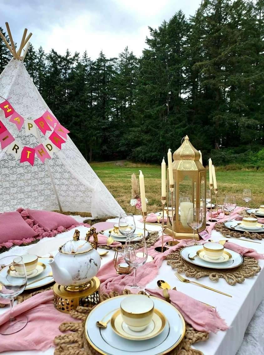 Birthday picnic with pink styling, tea set and Happy Birthday banner among evergreens
