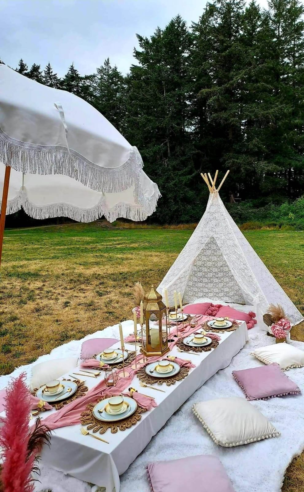 Cream fringe umbrella and lace teepee over a low picnic table in a meadow