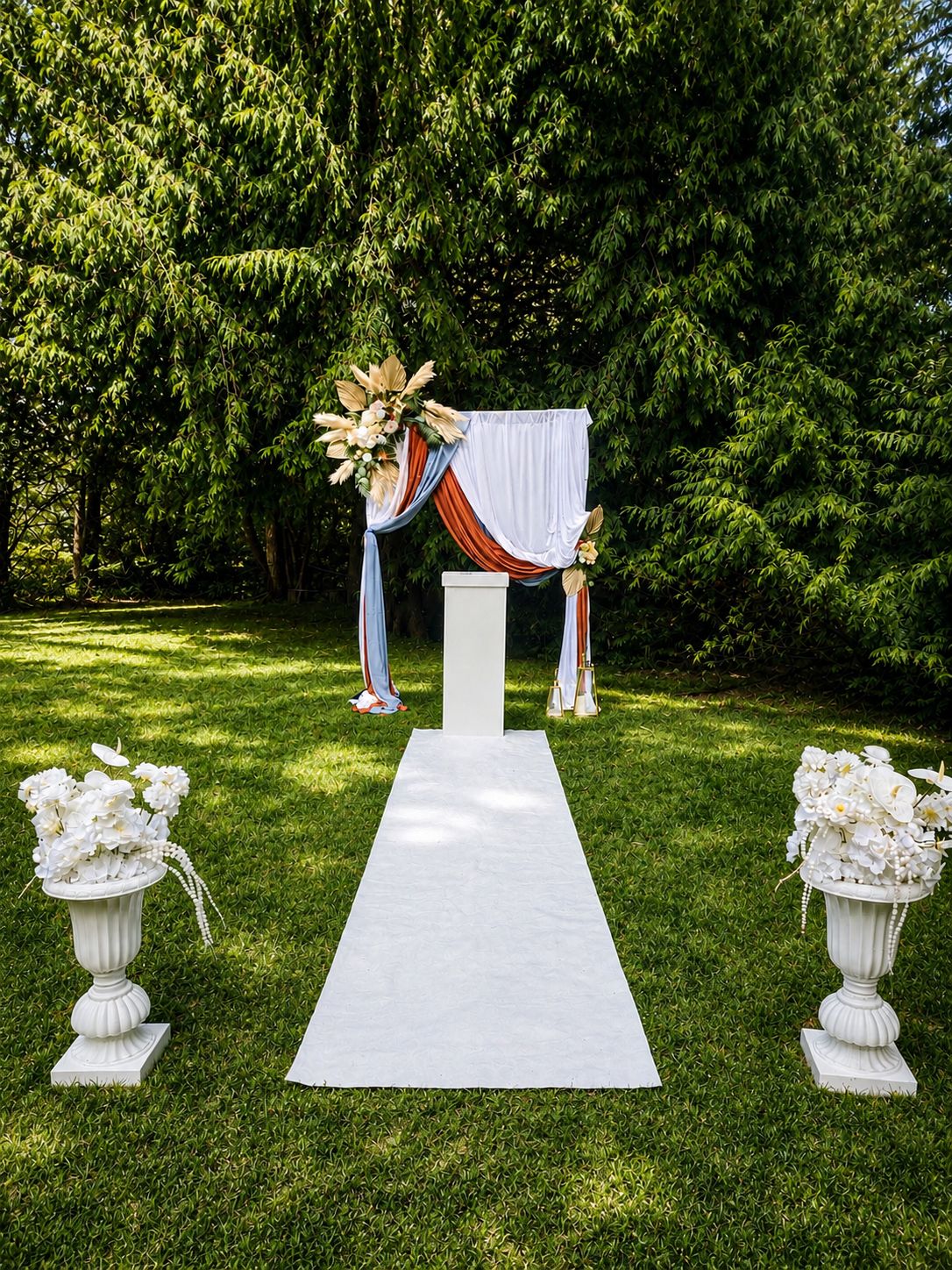 An outdoor wedding ceremony arch draped in terracotta and dusty blue with an aisle runner