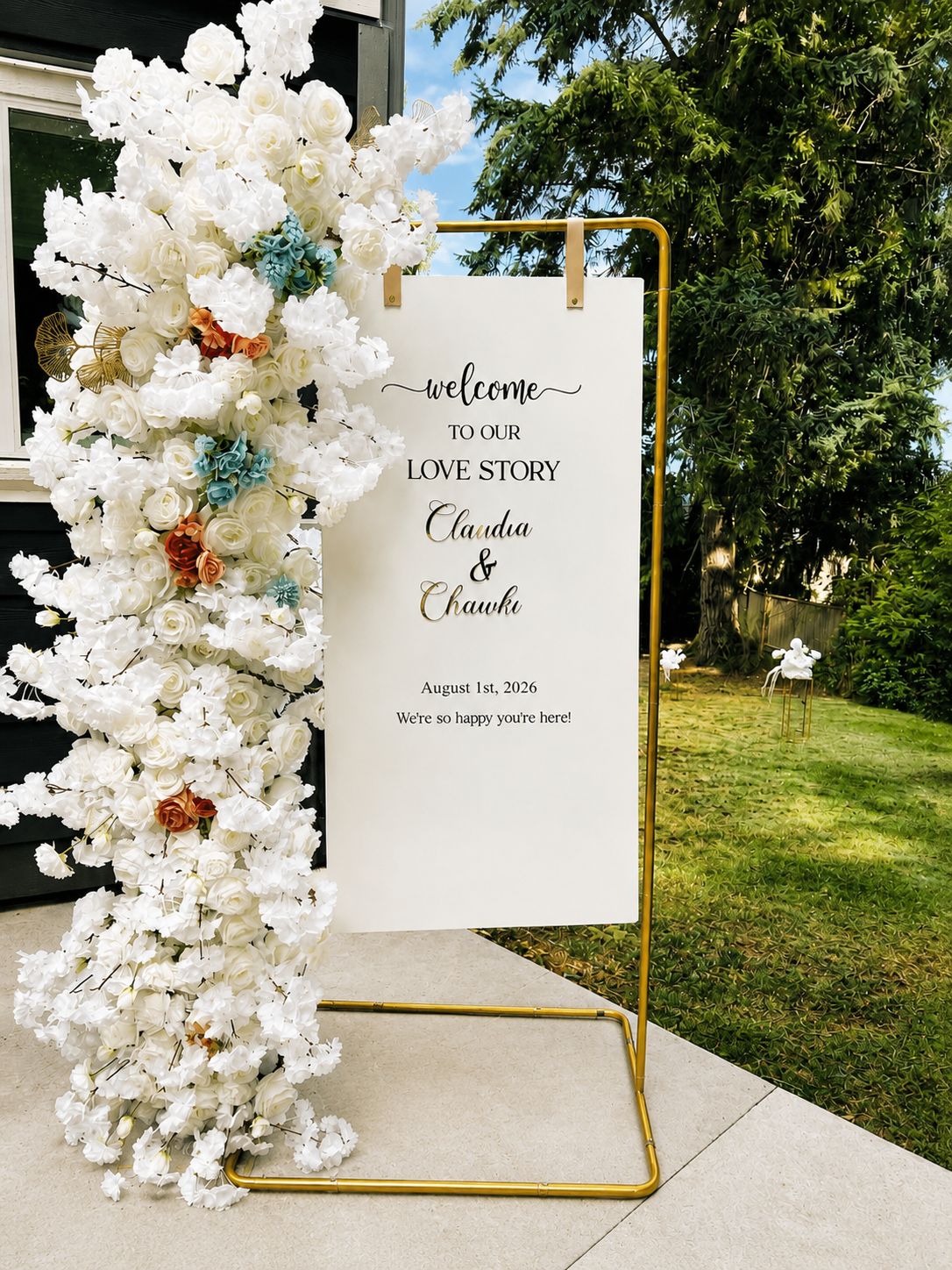 A personalised wedding welcome sign on a gold stand with a white and blush floral garland